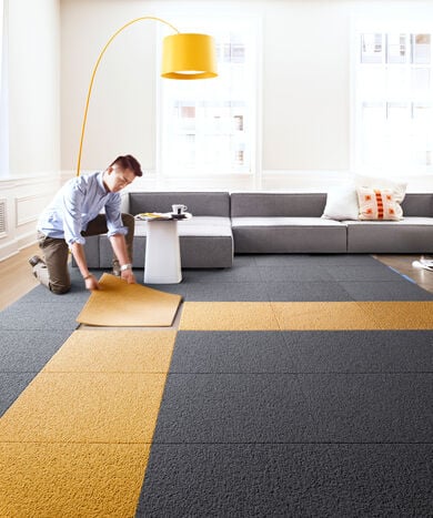 Man installing custom FLOR area rug in a bright loft apartment