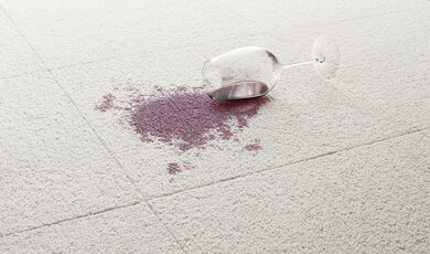 Close view of a spilled glass of red wine on a background of white FLOR carpet tiles. 