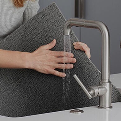 Hands of a person rinsing a gray FLOR carpet tile in a sink. 