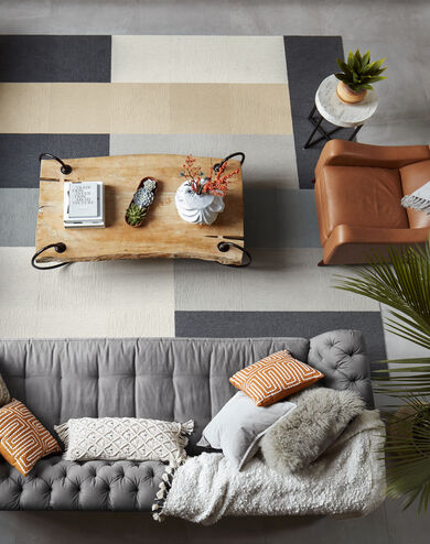 Overhead view of a gray couch, brown chair, metal table, metal side table, and FLOR Made You Look area rug in Bone, Granite, Flannel Blue, Eggnog, and Chalk. 