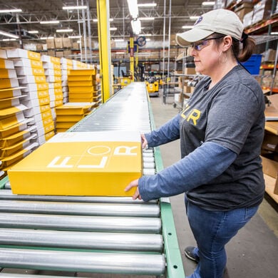 FLOR employee inspecting carpet tile box on a roller conveyor table