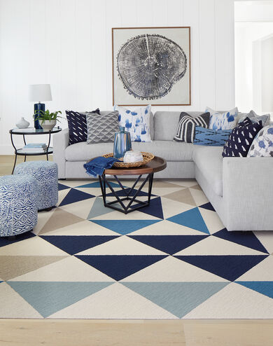 FLOR Made You Look area rug in Beige, Bone, Indigo, Tidal, and Flannel Blue, a white couch, blue printed ottomans, and metal tables.