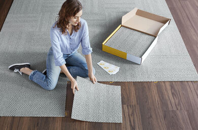 Woman installing FLOR tiles on a wood floor using FLORdots.