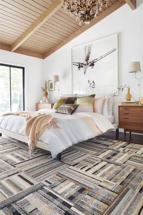 Better Half bedroom area rug in Blush, shown with a white bed and wood furniture.   