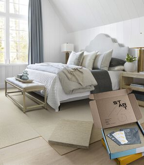 Bedroom with FLOR rug installation in progress, with stack of carpet tiles and open box.