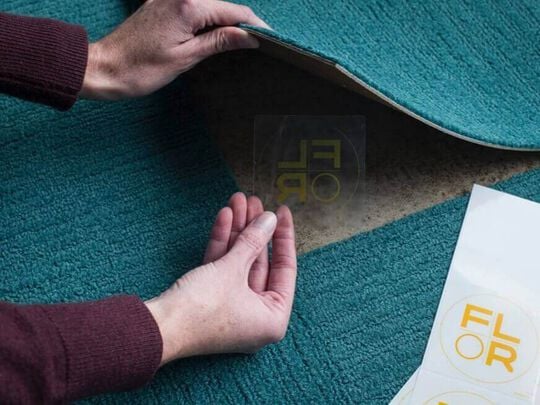 Hands of a person using a FLORdot to assemble a FLOR area rug from carpet tiles.