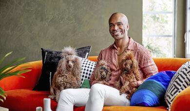 Travis London sitting on orange couch with his three poodles
