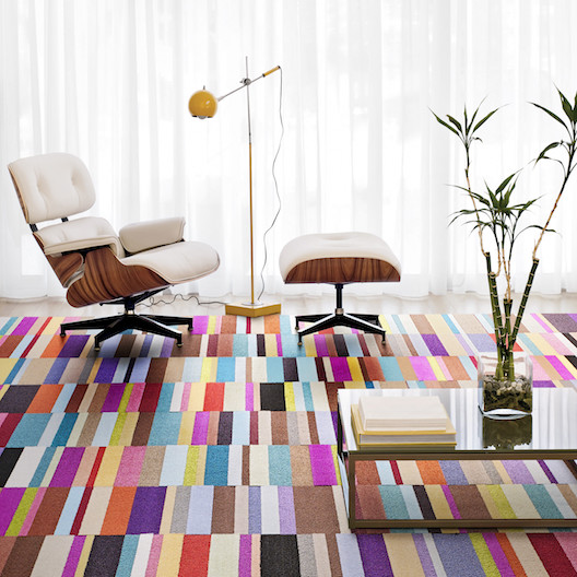 FLOR Parallel Reality home office area rug, a white and wood mid-century modern chair and footrest, and a yellow standing lamp. 